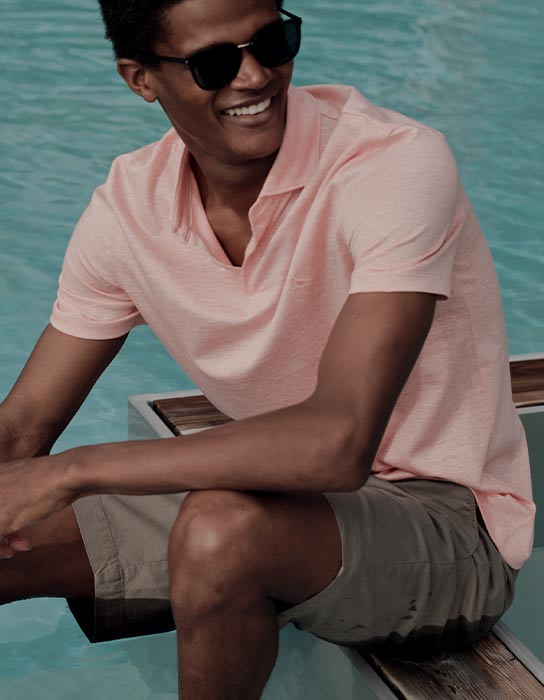 Man in olive green shorts and pink polo shirt sitting poolside