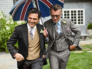 Two men in morning suits holding a union jack umbrella